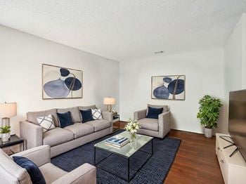 A living room with a grey couch, a glass coffee table, and two framed artworks on the wall